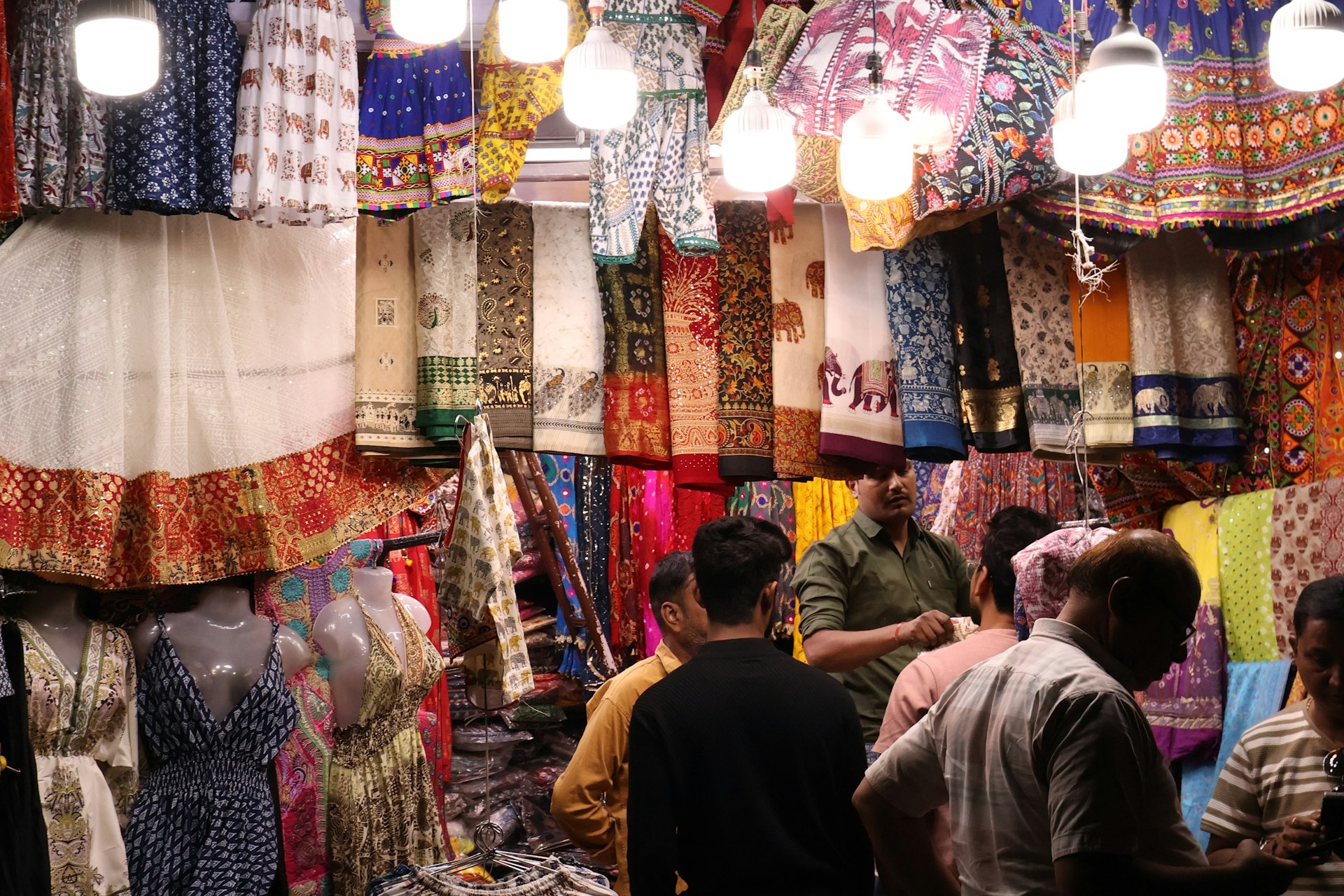 A shopkeeper showing garments to customers at a busy Indian cloth store